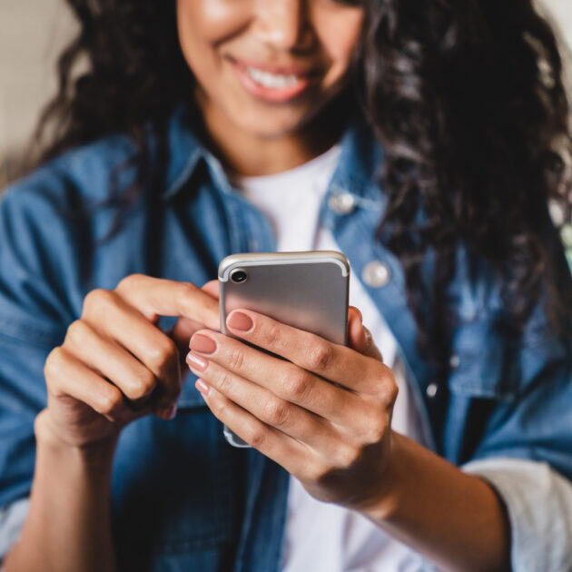 A person in a denim jacket smiles while using a smartphone.